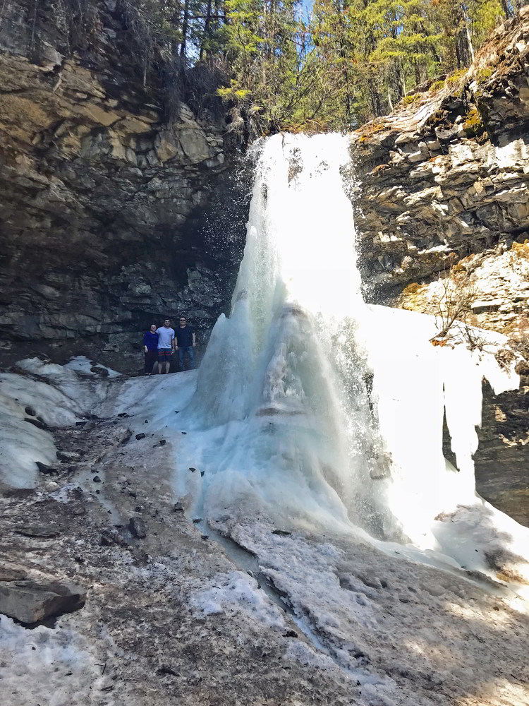 An image of three people standing behind the frozen Troll Falls in Kananaskis, Alberta