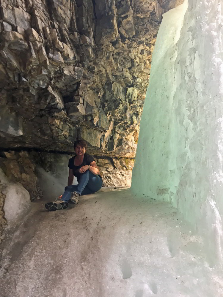 An image of a woman sitting behind the frozen Troll Falls in Kananaskis, Alberta