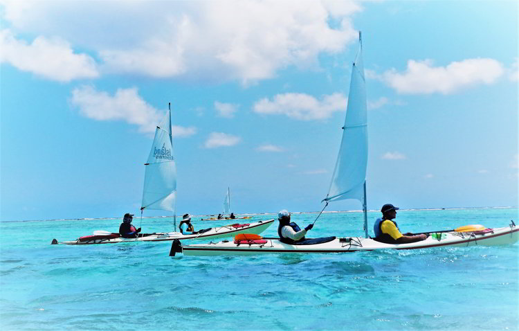 An image of three kayaks with sails sailing in Belize through the South Water Caye Marine Reserve