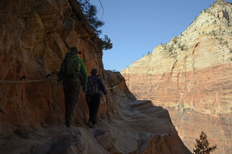 An image of two people grasping a chain as they climb the trail to Hidden Canyon Trail in Zion National Park in Utah - Best Zion National Park Hikes