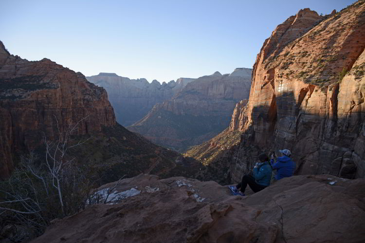 An image of two people sitting on the cliffs a sunset at Canyon Overlook in Zion National Park in Utah - Best Zion National Park Hikes