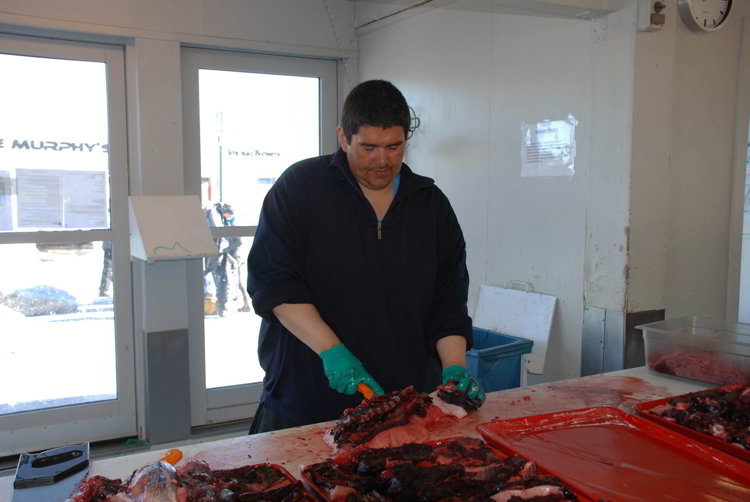 An image of a buthcre cutting up fish at the Ilulissat Fish Market in Ilulissat Greenland