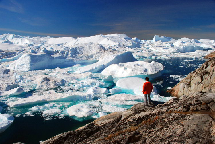 An image of a woman standing on a rock overlooking the Ilulissat Icefjord in Ilulissat Greenland