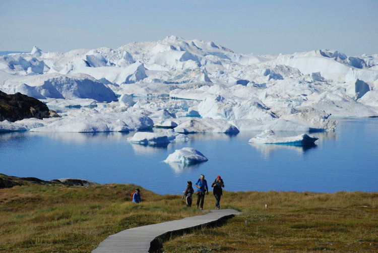 An image of three people walking on th boardwalk to reach the Ilulissat Icefjord in Ilulissat, Greenland 
