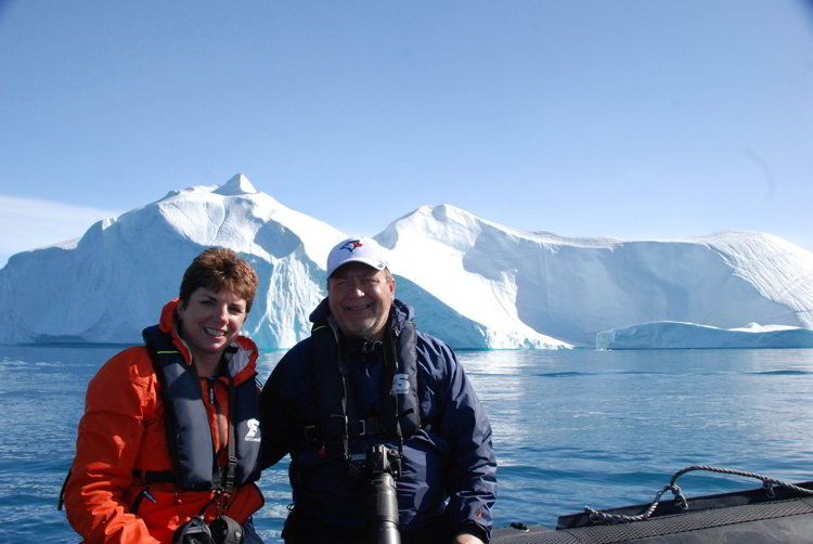 Two people sitting on a zodiac with an iceberg behind them near Ilulissat Greenland
