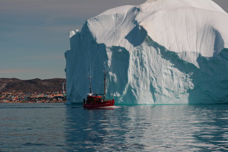 An image of a boat, a massive iceberg and the town of Ilulissat Greenland