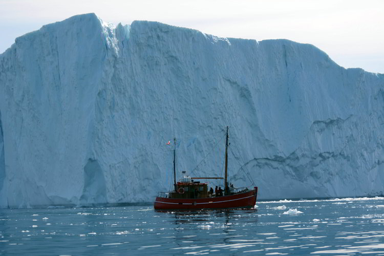 An image of a wooden boat in front of a large iceberg near Ilulissat Greenland