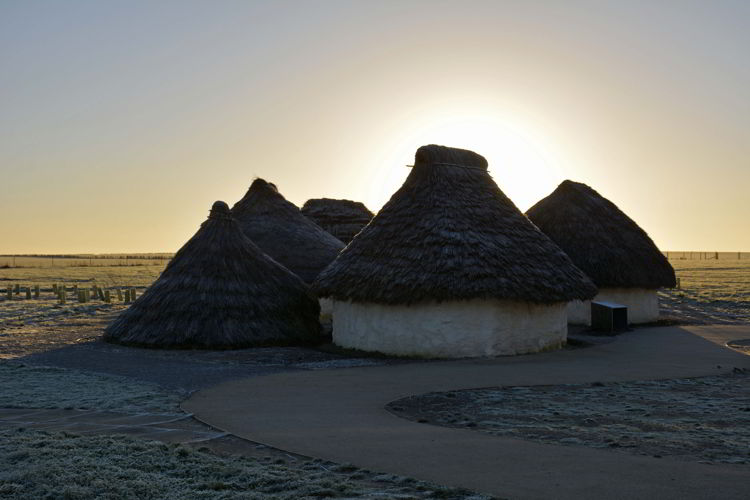 An image of the sunrise over the reconstructed Neolithic houses at the Stonehenge site near Salisbury, UK - Stonehenge inner circle tours
