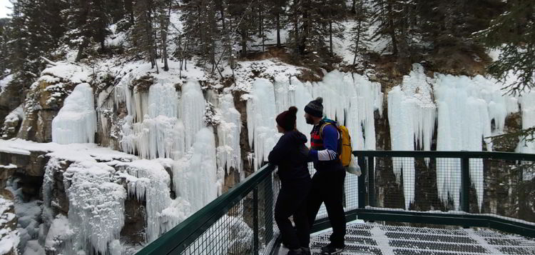 An image of a couple looking at ice formations in Johnston Canyon above the upper falls in Banff National Park, Alberta - Johnston Canyon Winter Hike and ink pots hike
