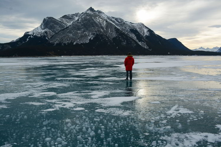 An image of a man standing on Abraham Lake in winter with ice bubbles in the foreground - Abraham Lake, Alberta