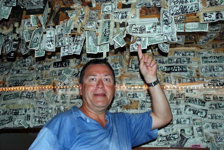 An image of a man pointing at a $1 bill he attached to the ceiling of the restaurant at Cabbage Key Inn and Restaurant - Cabbage Key Cheeseburger in Paradise