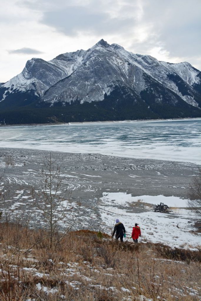 An image of two people walking down to the frozen Abraham Lake, Alberta. 