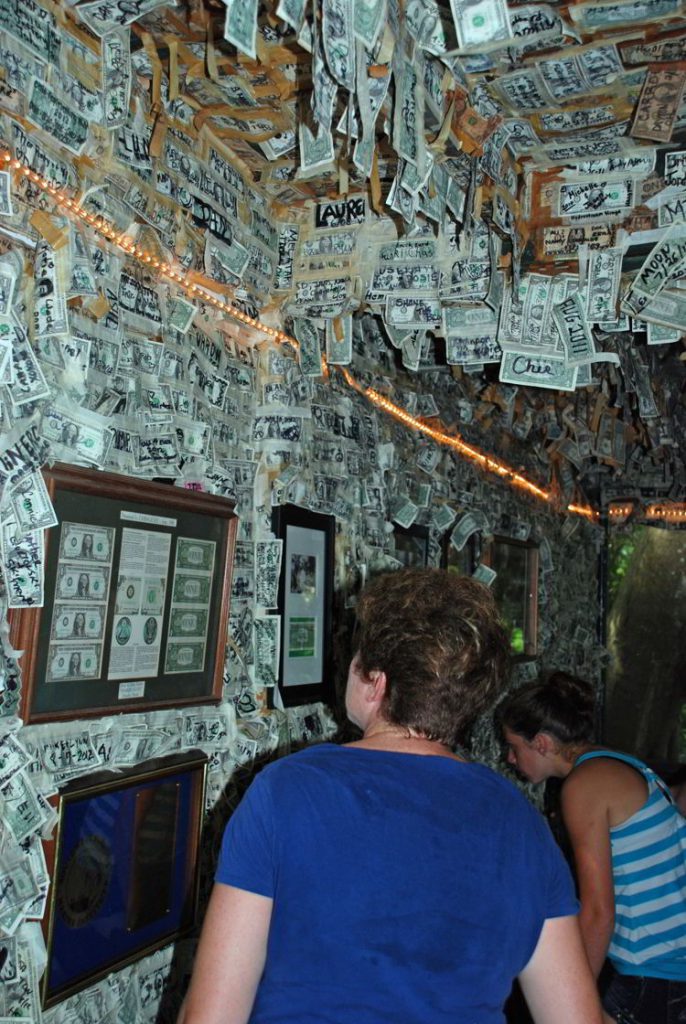 An image of a woman walking by the pictures of famous people putting $1 bills on the wall at Cabbage Key Inn and Restaurant - Cabbage Key cheeseburger in paradise