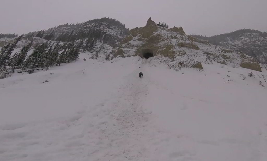 An image of a hiker climbing up a snowy hill to a cave on the Grotto Canyon hike near Canmore, Alberta