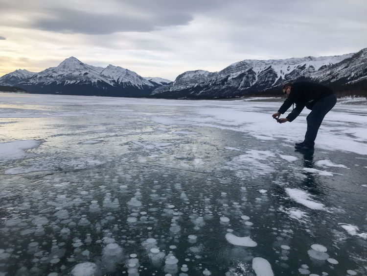 An image of a man taking a photograph of the ice bubbles in Abraham Lake, Alberta
