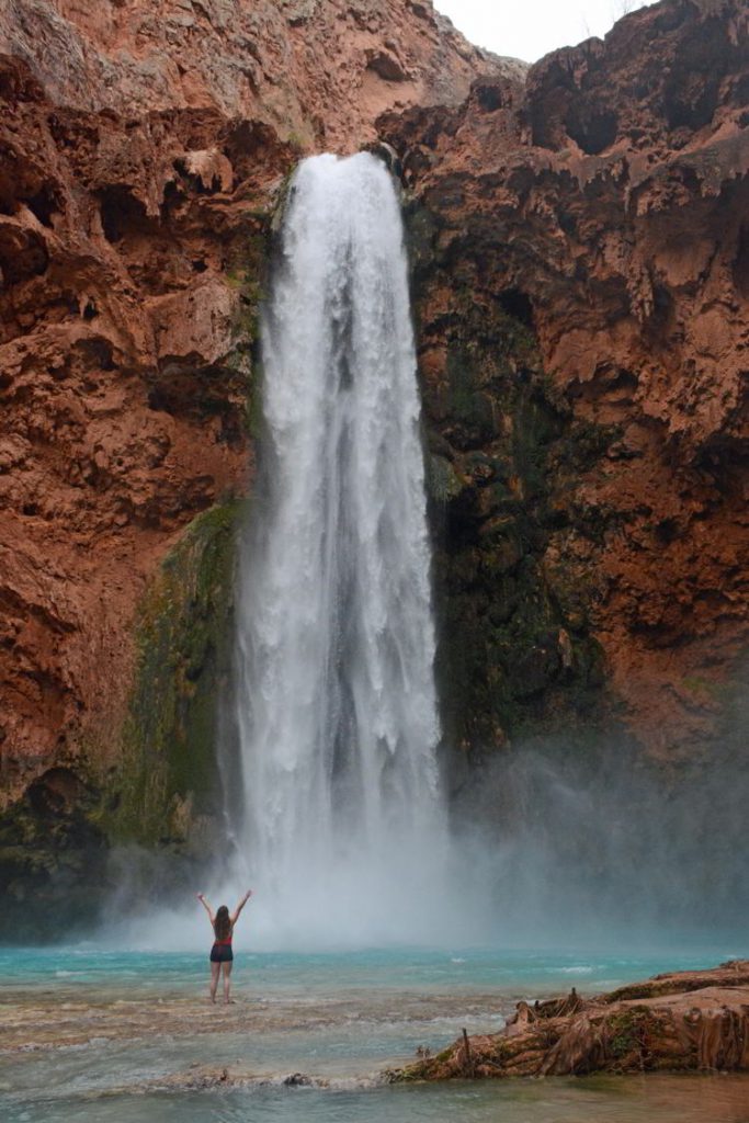 An image of a woman standing in front of Mooney Falls - Havasupai Hike