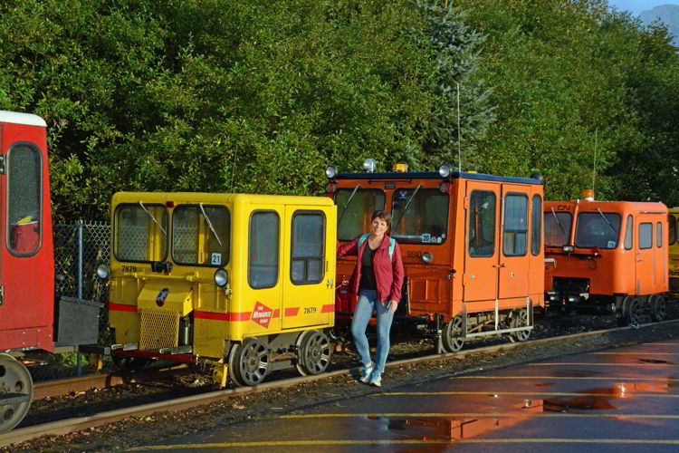 An image of a woman standing in front of some colorful rail motor cars in Seward, Alaska USA