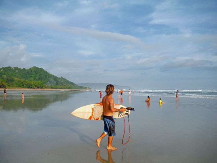 An image of a local carrying his surfboard to the beach to go surfing at Playa Hermosa in Costa Rica