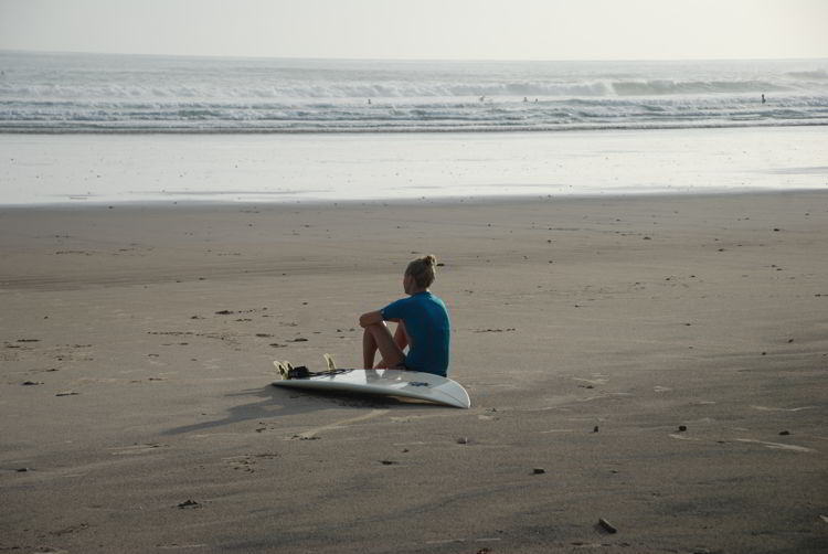 An image of a woman sitting on the beach with her surfboard in Costa Rica. 