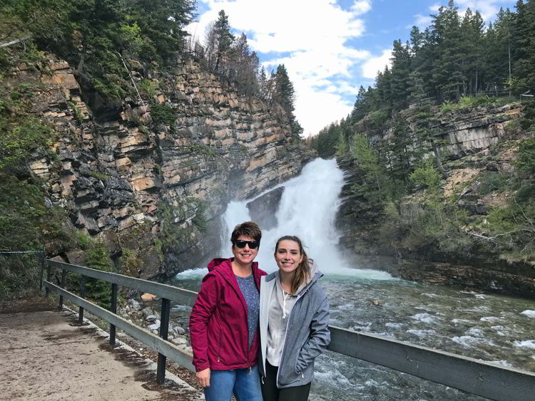 An image of two women standing in front of Cameron Falls in Waterton Lakes National Park in Alberta, Canada. 