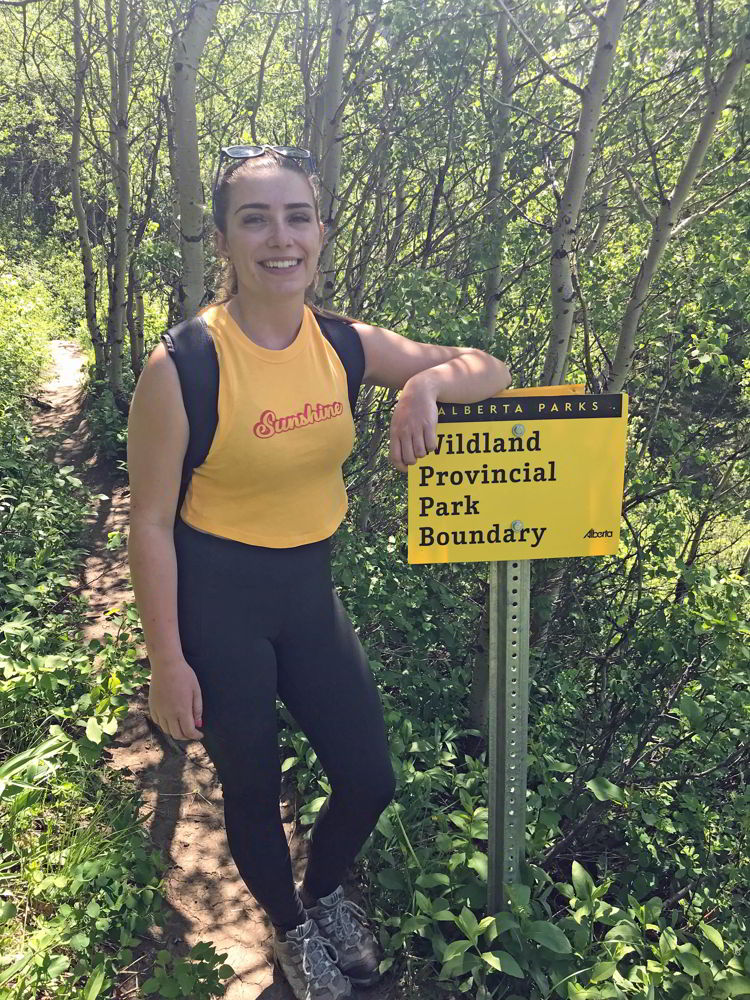 An image of a young woman standing beside the sign for Castle Wildland Provincial Park in Alberta, Canada. 