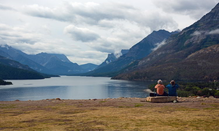 An image of two people taking in the view from the bluff behind the Prince of Wales Hotel in Waterton Lakes National Park in Alberta, Canada. 