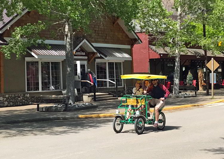 An image of a dad and his two daughters riding a surry bike in downtown Waterton