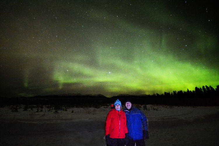 An image of two people standing in front of the Yukon northern lights outside Whitehorse in January. 