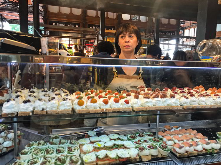 An image of a tapas vendor standing behind a counter at the Mercado de San Miguel in Madrid, Spain.