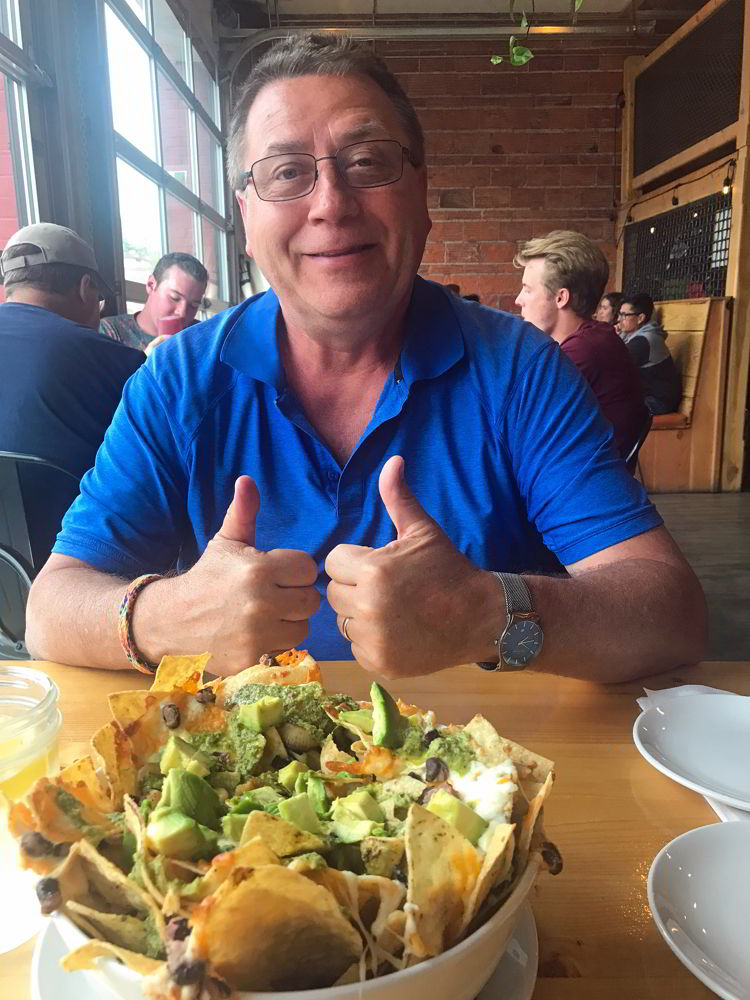 An image of a man giving two thumbs up to the nachos at Fire Hall Kitchen & Tap in Cranbrook, BC.  