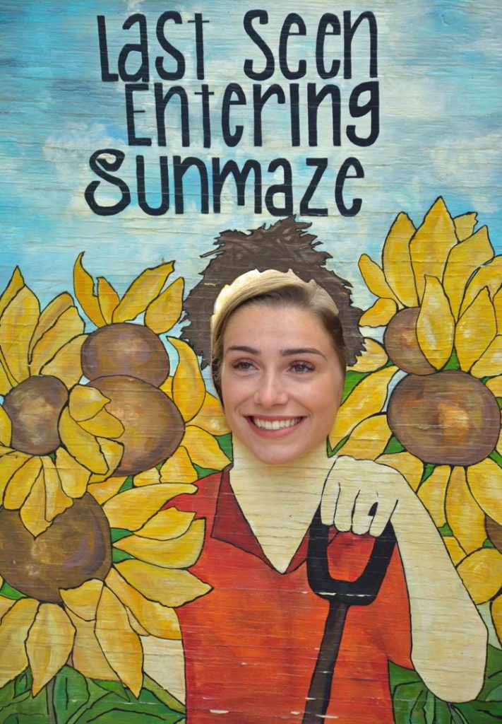 An image of a girl poking her head through a sign at the Bowden Sunmaze in Bowden, Alberta, Canada. 