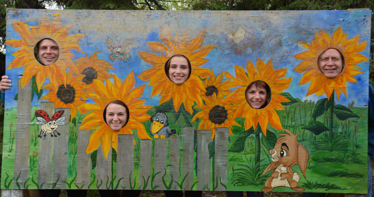 An image of a group of people with their heads poking through the Bowden Sunmaze sign in Bowden, Alberta, Canada. 