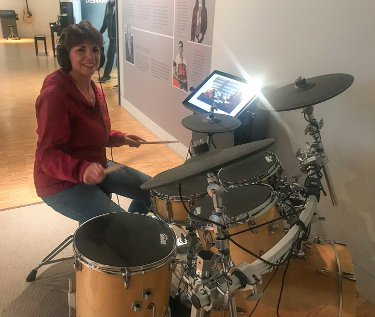 An image of a woman wearing headphones and playing a drum set. 