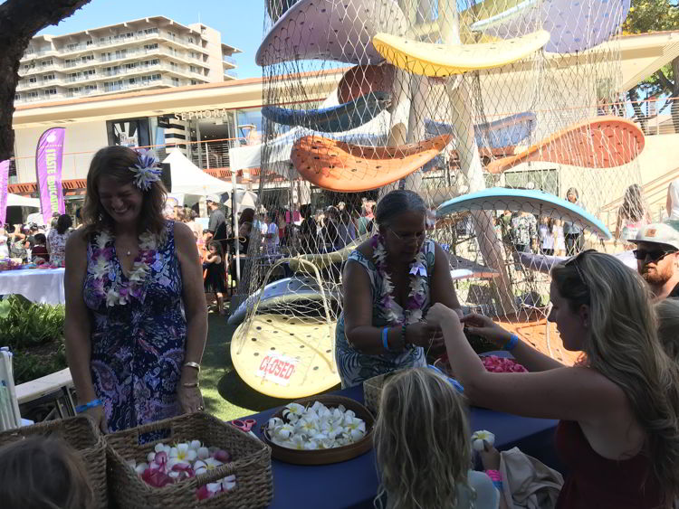 An image of children making flower leis at the Keiki in the Kitchen event of the Hawaii Food and Wine Festival in Kāʻanapali, Maui.  
