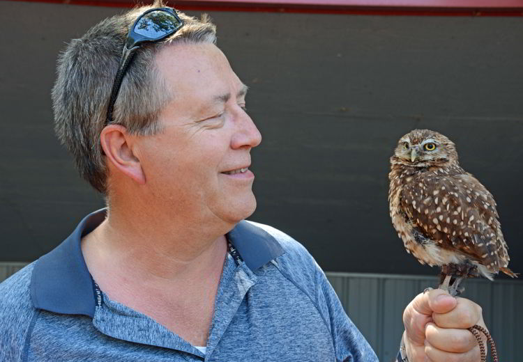 An image of a man holding a burrowing owl at the Alberta Birds of Prey Centre near Lethbridge, Alberta. 