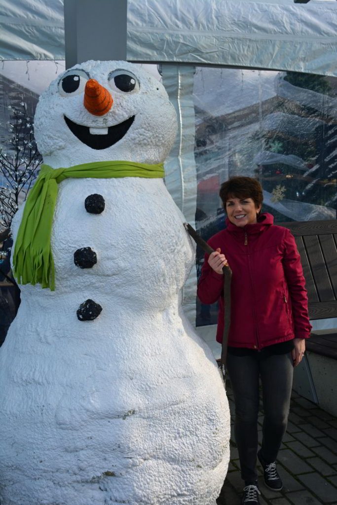 An image of a woman standing beside a snowman at the German Christmas Market in Vancouver, BC, Canada. 