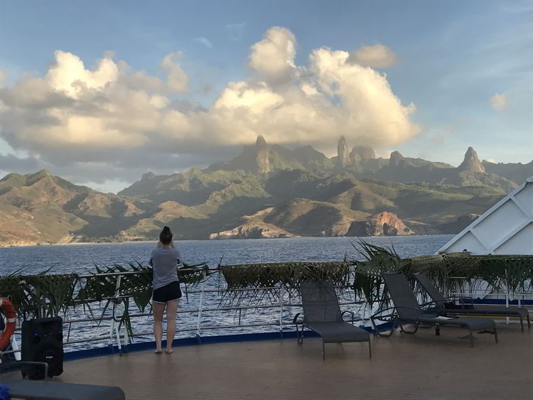 An image of a person standing on the deck of Aranui 5 looking at Ua Pou Island in the Marquesas Islands of French Polynesia.  