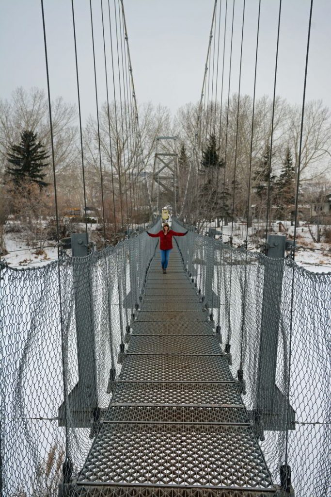 An image of a woman standing on the Star Mine Suspension Bridge near Drumheller, Alberta in the winter. 