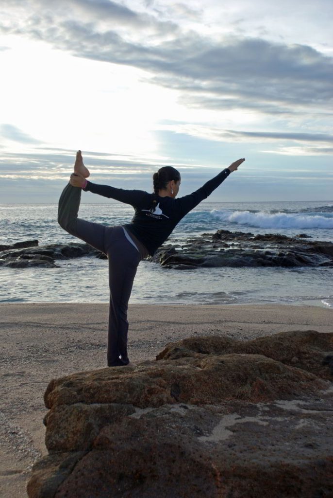 An image of a woman doing a yoga pose on the beach.
