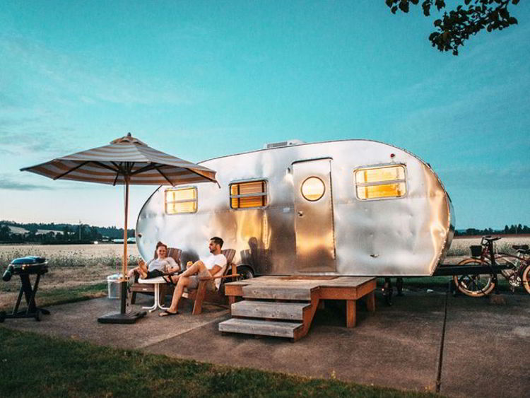 An image of two people sitting in front of a camping trailer - Ruckify - glamping in Alberta. 