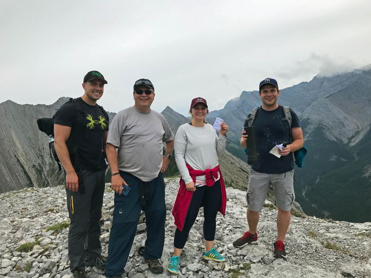 An image of four people holding the summit register on Grant MacEwan Peak near Canmore, Alberta. 