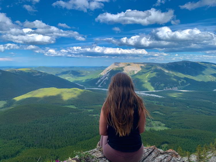 An image of a woman sitting at the top of Nihahi Ridge in Kananaskis Country in Alberta, Canada. 