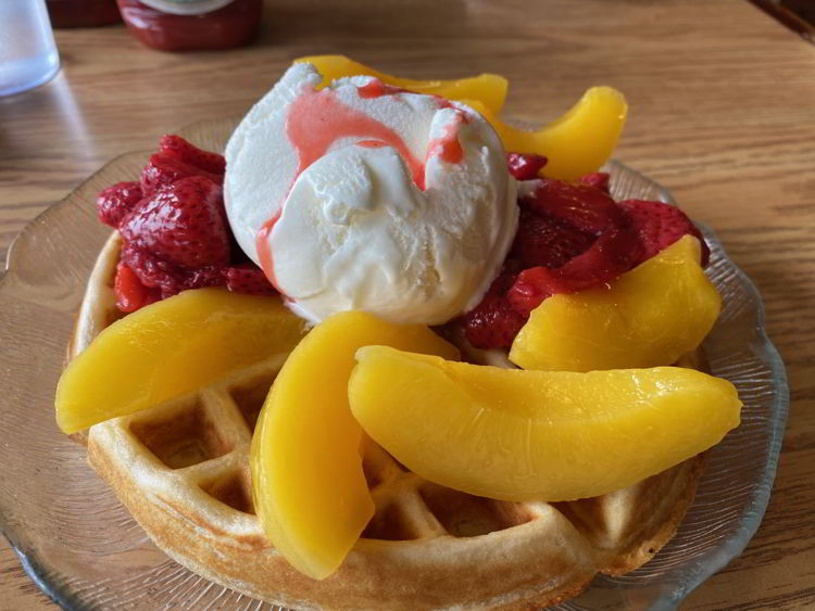 An image of a waffle with ice cream, peaches and strawberries. 