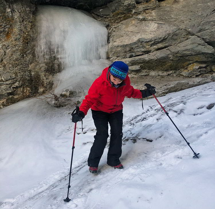 An image of a woman hiking up a frozen creek in Crowsnest Pass, Alberta, Canada. 