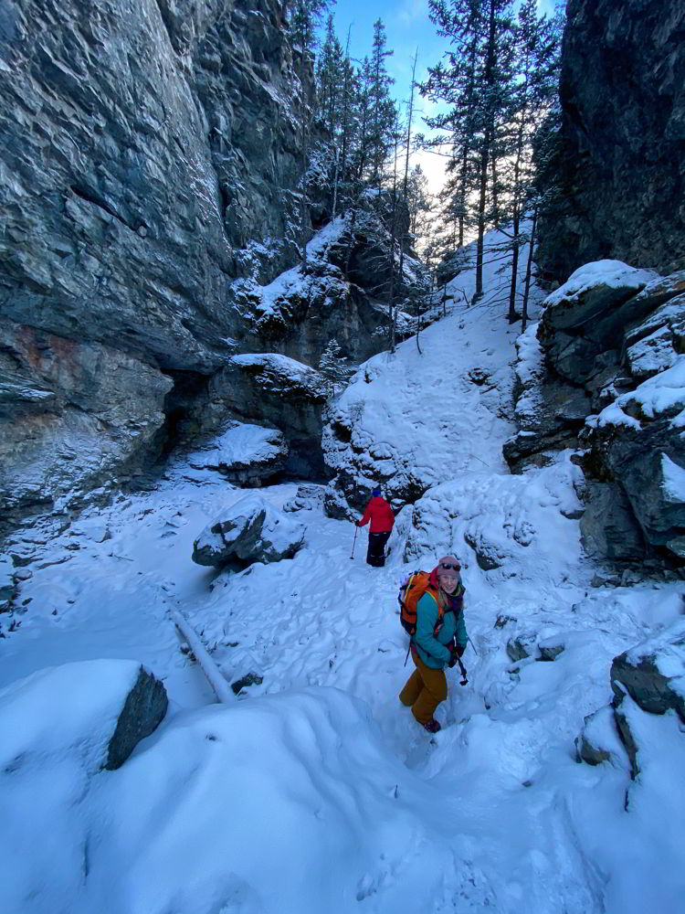 An image of two people hiking along the frozen creek on the Star Creek Falls ice walk in Crowsnest Pass, Alberta, Canada. 