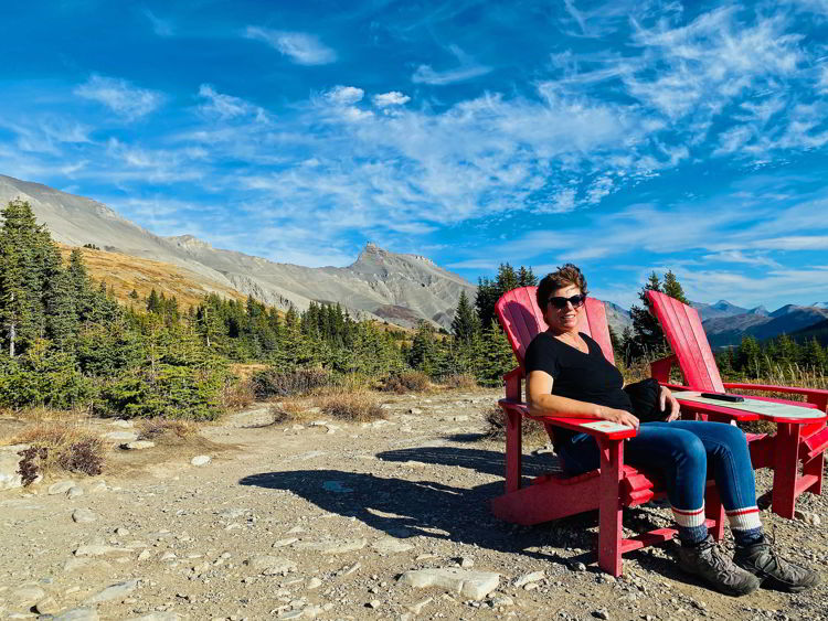 An image of a woman sitting in a Parks Canada red chair taking in the view of the Athabasca Glacier as seen from the Wilcox Pass trail on the Icefields Parkway in Jasper National Park in Alberta, Canada. 