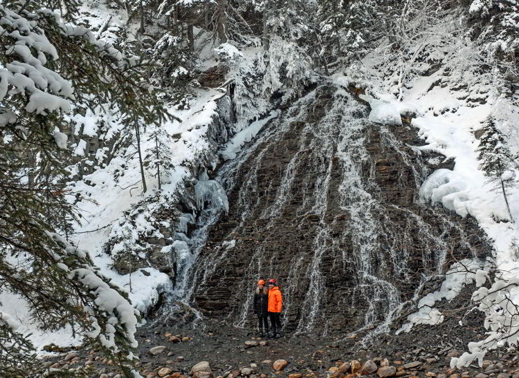 An image of a couple standing in front of a waterfall in Maligne Canyon in winter. 