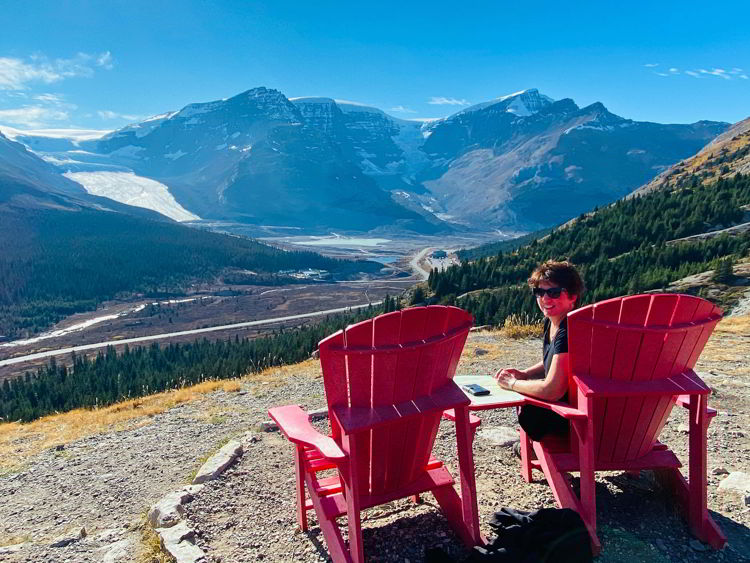 An image of a woman sitting in a Parks Canada red chair taking in the view of the Athabasca Glacier as seen from the Wilcox Pass trail on the Icefields Parkway in Jasper National Park in Alberta, Canada. 