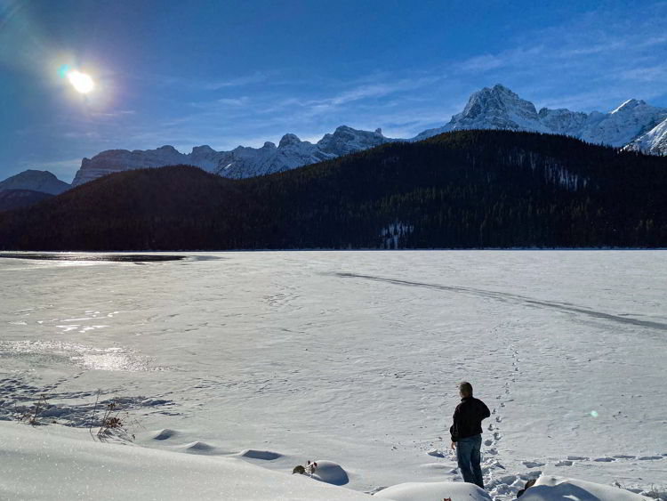 An image of a man standing on the shore of Bow Lake in winter in Banff National Park on the Icefields Parkway drive from Banff to Jasper, Alberta Canada. 