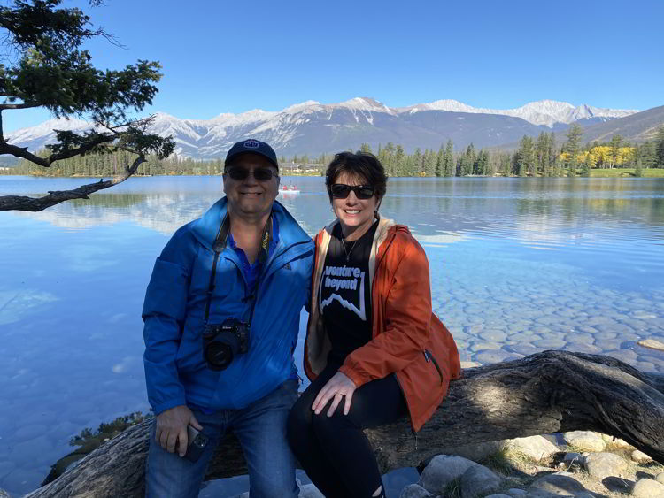 An image of a couple sitting on the edge of Lac Beauvert in Jasper National Park in Alberta, Canada.